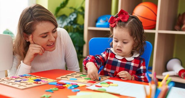 Maestro y niño pequeño jugando con las matemáticas juego de puzzle sentado en la mesa en el jardín de infantes - Foto, imagen