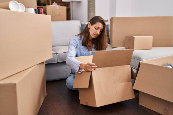 Young woman moving to a new home looking inside cardboard box depressed and worry for distress, crying angry and afraid. sad expression.  - Foto, imagen