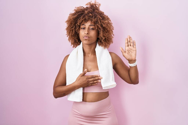 Young hispanic woman with curly hair wearing sportswear and towel swearing with hand on chest and open palm, making a loyalty promise oath  - Photo, Image