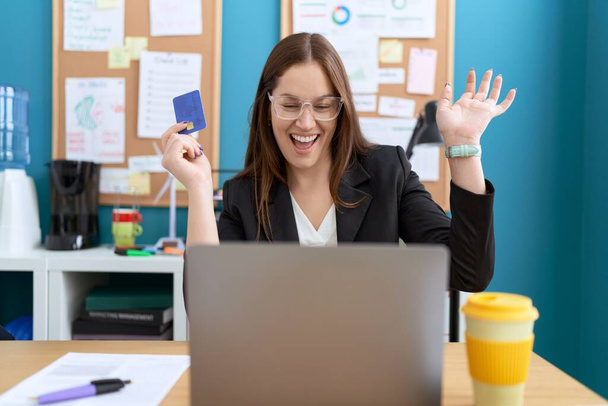Young beautiful woman business worker using laptop holding credit card with celebration expression at office - Foto, Bild