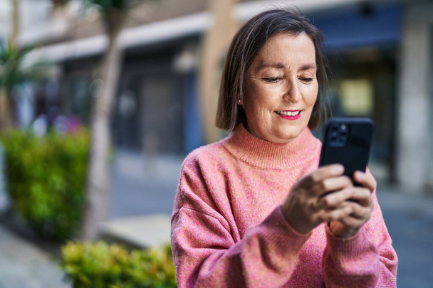 Middle age woman smiling confident using smartphone at street - Fotó, kép