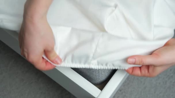 Op het matras van het bed wordt een wit satijnen laken met elastiek aangebracht, een close-up van de handen. Beddengoed - Video