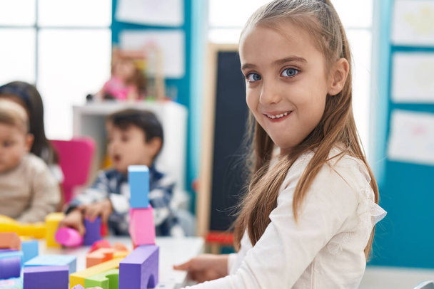 Urocza latynoska dziewczyna bawiąca się klockami budowlanymi siedzącymi na stole w przedszkolu - Zdjęcie, obraz