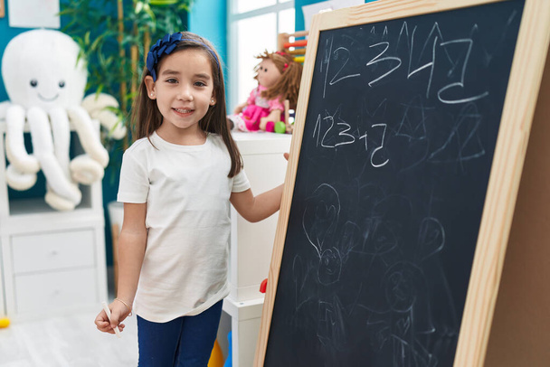 Adorable hispanic girl preschool student smiling confident writing numbers on blackboard at kindergarten - Fotografie, Obrázek
