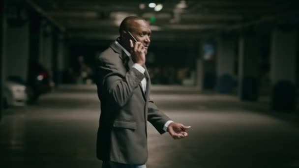 Preocupado hombre afroamericano maduro caminando en el estacionamiento hablar en el teléfono móvil frustrado empresario estresado discutir el problema de negocios utilizando el teléfono inteligente caminar en garaje subterráneo hablar por teléfono celular - Metraje, vídeo