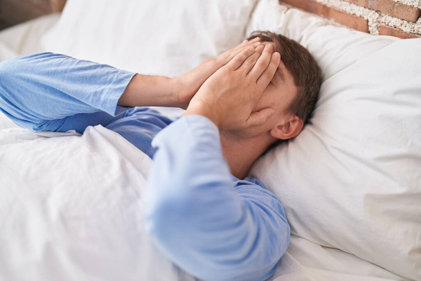 Νεαρός καυκάσιος άνδρας στρεσαρισμένος ξαπλωμένος στο κρεβάτι - Φωτογραφία, εικόνα