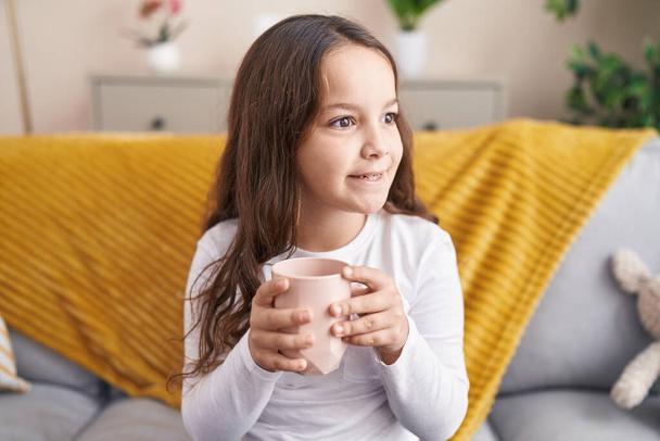 Imádnivaló spanyol lány iszik csésze tejet ül a kanapén otthon - Fotó, kép