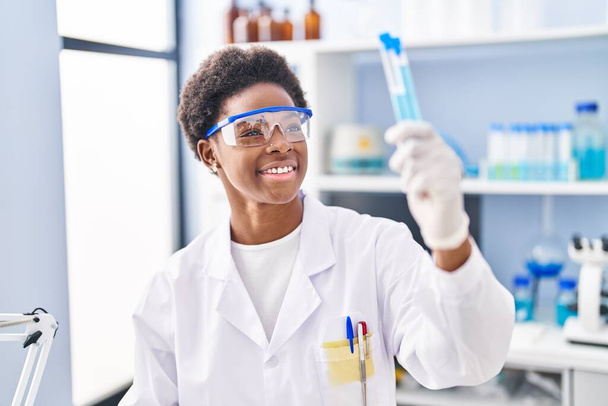 African american woman wearing scientist uniform holding test tubes at laboratory - Foto, Bild