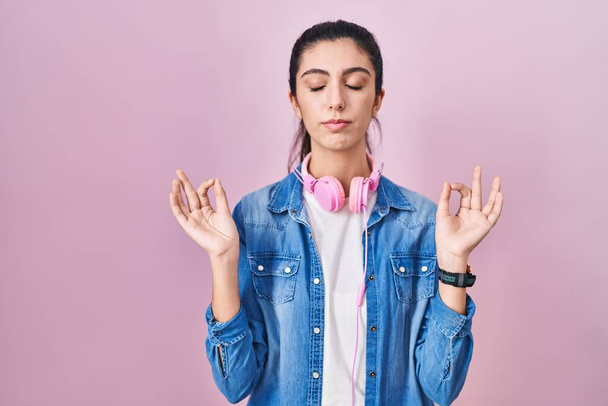 Young beautiful woman standing over pink background relax and smiling with eyes closed doing meditation gesture with fingers. yoga concept.  - 写真・画像