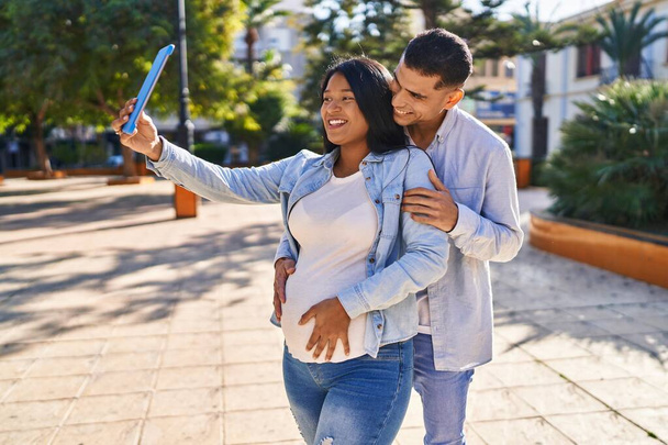 Junges lateinisches Paar erwartet Baby beim Selfie mit dem Touchpad im Park - Foto, Bild