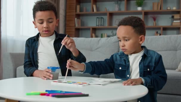 Two African American creative smart concentrate little children boys painting at home together with paints ethnic brothers kids sibling paint picture with acrylic watercolor colors art hobby education - Séquence, vidéo