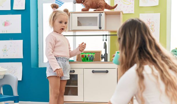 Teacher and toddler playing with play kitchen standing at kindergarten - 写真・画像