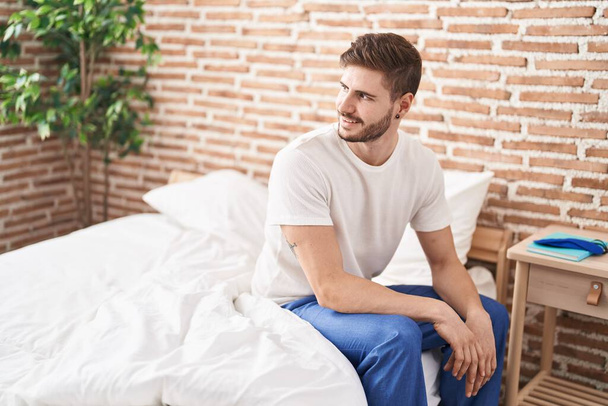 Giovane uomo caucasico sorridente fiducioso seduto sul letto a camera da letto - Foto, immagini