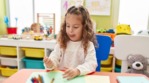 Чарівна блондинка малюк дошкільного віку сидить на столі малює на папері в дитячому садку
 - Фото, зображення