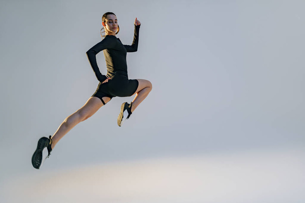 Athletic active woman jumping on studio background. Dynamic movement - Zdjęcie, obraz