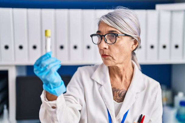 Middle age grey-haired woman scientist holding test tube at laboratory - Photo, Image