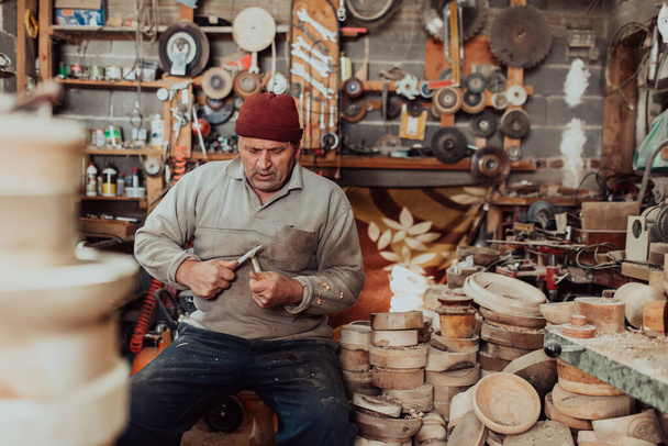 Starszy mężczyzna siedzi w warsztacie i przetwarza drewniane naczynia w stary, ręczny sposób..  - Zdjęcie, obraz