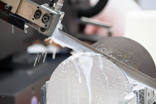 Toiminta vannesahan leikkurit leikkaamalla metalliakselin osat jäähdytysnesteen menetelmällä. Teollisuuskäyttöön tarkoitettu työstökone. - Valokuva, kuva