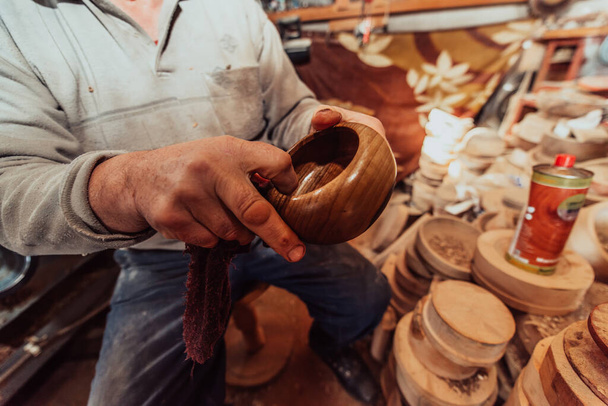 A senior man sitstingin the workshop and smearsing wooden utensils with linseed oil.  - Foto, imagen