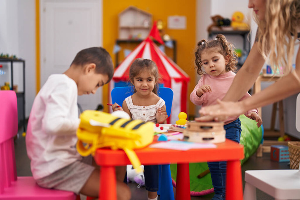 Группа детей дошкольников, сидящих на бумажном столе в детском саду - Фото, изображение