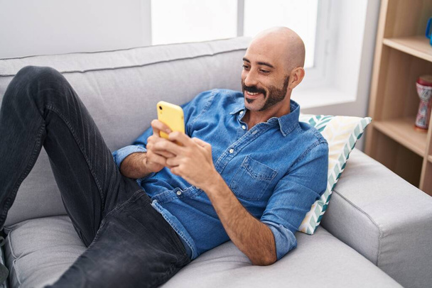 Nuori latino mies käyttää älypuhelin makaa sohvalla kotona - Valokuva, kuva