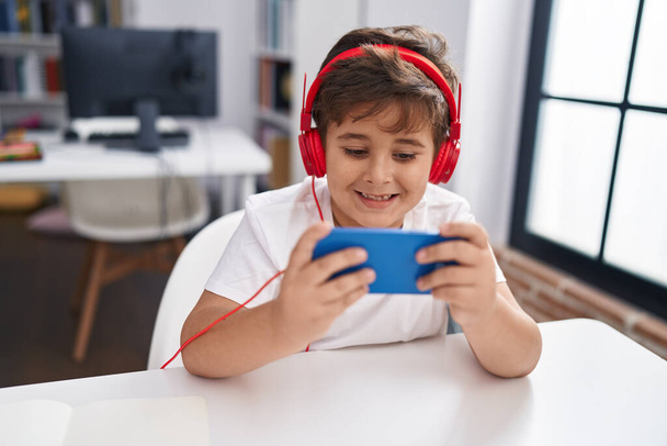 Чарівний студент іспаномовного хлопчика використовує смартфон та навушники в класі
 - Фото, зображення