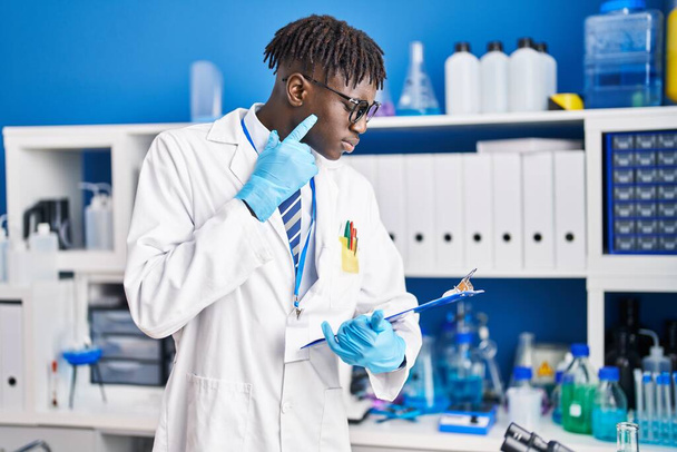Hombre científico afroamericano leyendo informe con expresión de duda en laboratorio - Foto, imagen