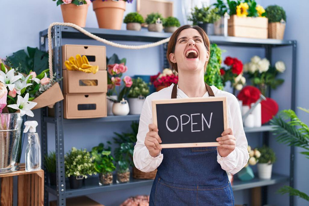 Brunette woman working at florist holding open sign angry and mad screaming frustrated and furious, shouting with anger looking up.  - Photo, Image