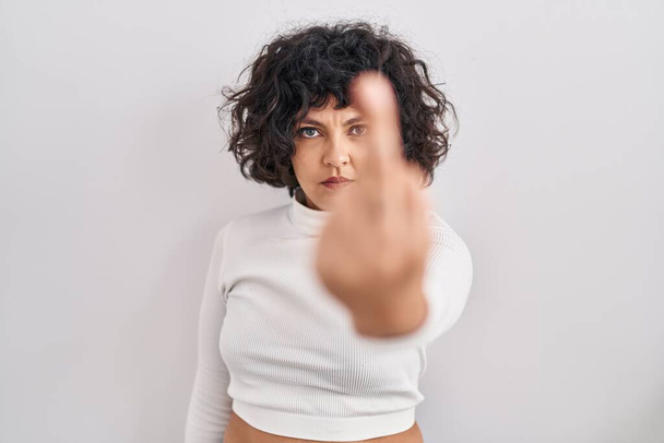 Hispanic woman with curly hair standing over isolated background showing middle finger, impolite and rude fuck off expression  - Photo, image