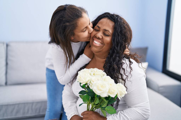 Mother and daughter surprise with flowers sitting on sofa at home - Photo, Image