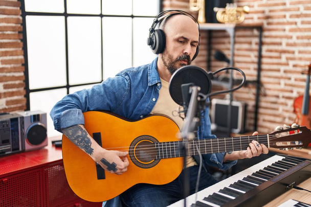 Young bald man musician singing song playing classical guitar at music studio - Photo, Image