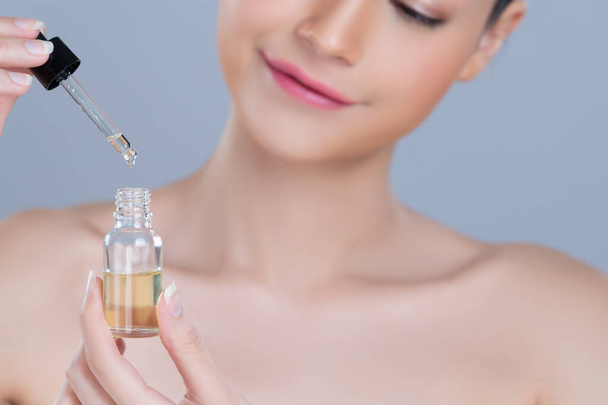 Focus cannabis extracted oil bottle with dropper lid holding by blurred glamorous beautiful asian woman with perfect clean skin and soft smooth makeup in isolated background. - Φωτογραφία, εικόνα