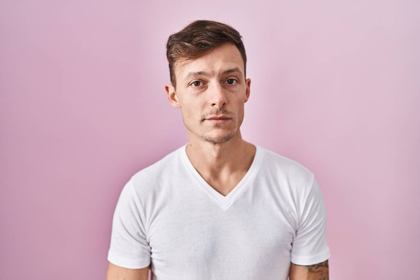 Caucasian man standing over pink background relaxed with serious expression on face. simple and natural looking at the camera.  - Zdjęcie, obraz