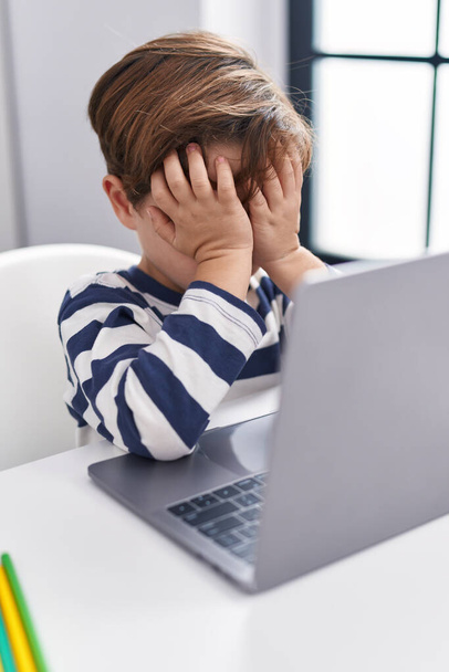 Adorable hispanic boy student using computer with stressed expression at classroom - Photo, image