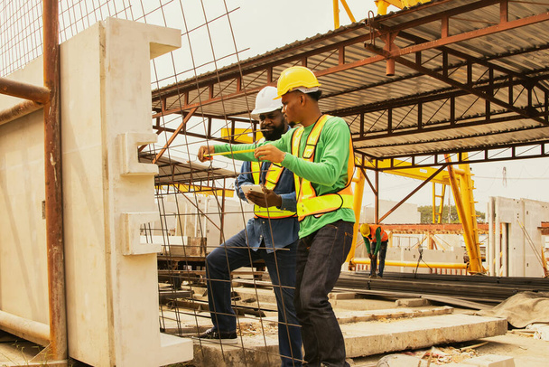 African American foremen and Asian workers use tape measure measure rebar spacing check strong and stable standards and record their work on a tablet for the construction of precast concrete walls. - Photo, Image