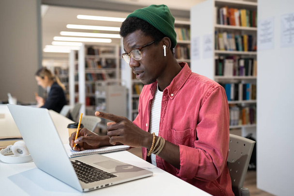 Concentré homme étudiant afro-américain concentré dans les écouteurs regarder la connexion à l'écran de l'ordinateur portable, discuter de matériel didactique ou d'études de langue étrangère avec le professeur tuteur en utilisant appel vidéo. - Photo, image