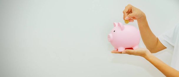 Banner side view : Young woman's hand holding piggy bank and gold coin to promote future savings. business, Investment, retirement, insurance. education : Saving money concept. - Foto, imagen