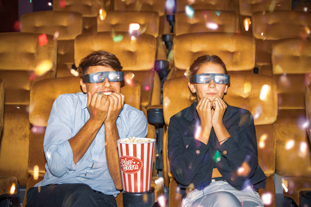 Paar legt Popcorn auf einen Stuhl, trägt 3-D-Brille, sitzt und schaut sich Multiplex-Film in einem abenteuerlichen Kino an und betrachtet die Szene, die es dem Helden ermöglicht, den Bösewicht mit beiden aufregenden Herzen zu besiegen. - Foto, Bild
