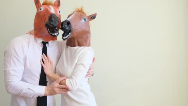 Ένας άντρας και μια γυναίκα με μάσκα αλόγου χορεύουν και διασκεδάζουν σε ελαφρύ φόντο. Αστείο ζευγάρι που διασκεδάζει. - Πλάνα, βίντεο