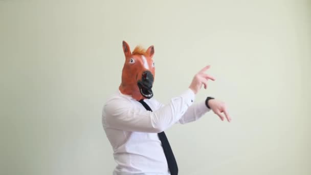 A funny man in a strange carnival horse mask is dancing and having fun on a light background in the studio. Horse masquerade mask. - Video, Çekim