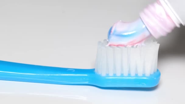 Gekleurde tandpasta wordt aangebracht op een borstel op een witte achtergrond close-up. Tandheelkundige zorg. Blauwe wijting - Video