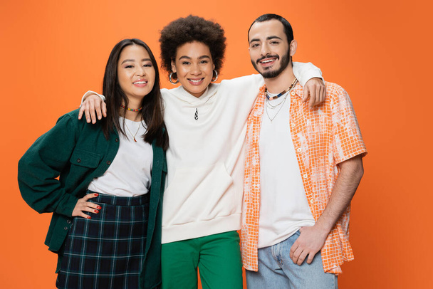 cheerful african american woman embracing trendy multiracial friends isolated on orange - Fotoğraf, Görsel