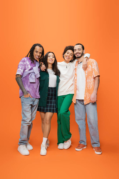 full length of happy african american woman embracing stylish multicultural friends on orange background - Photo, image