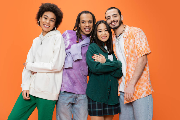 happy multiethnic friends wearing stylish clothes and posing isolated on orange - Fotó, kép