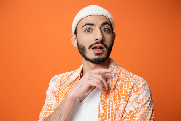 vaikuttunut parrakas mies trendikäs paita ja valkoinen pipo katsot kameraa eristetty oranssi - Valokuva, kuva