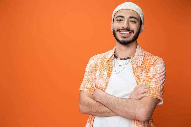 joyful bearded man in fashionable outfit posing with crossed arms isolated on orange - Foto, Imagem