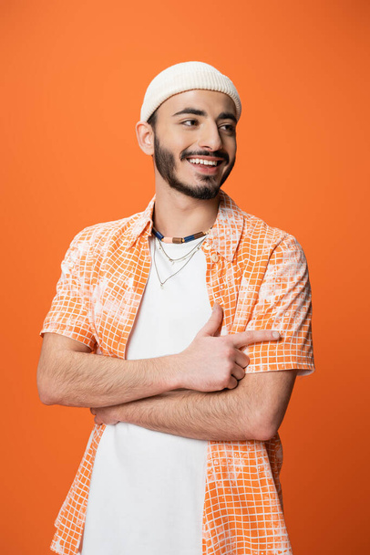 Havalı sakallı bir adam gülümseyip parmağıyla işaret ederken portakalda izole bir şekilde yüzünü çeviriyor. - Fotoğraf, Görsel