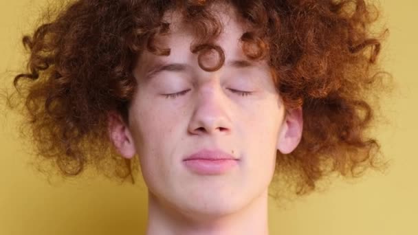 Close-up of the face of a curly red-haired boy, a student on a light brown background. The emotion of peace, happiness. Relaxation, meditation. A guy with narrowed eyes. - Footage, Video