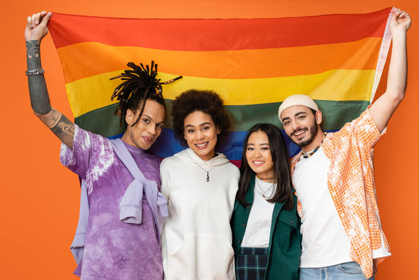 cheerful and trendy multiethnic friends posing with lgbt flag isolated on orange - Fotografie, Obrázek