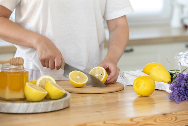 Egy fiatal nő citromot vág a deszkán. Friss emonádé előkészítése. Levendula és citrom - Fotó, kép